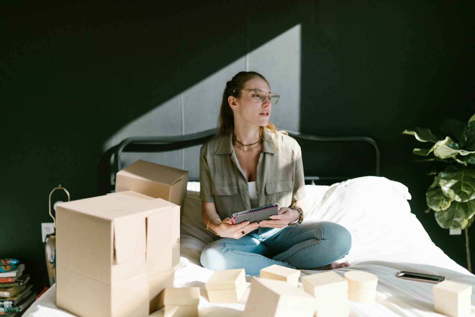 Woman working on e-commerce startup with tablet and boxes on bed.